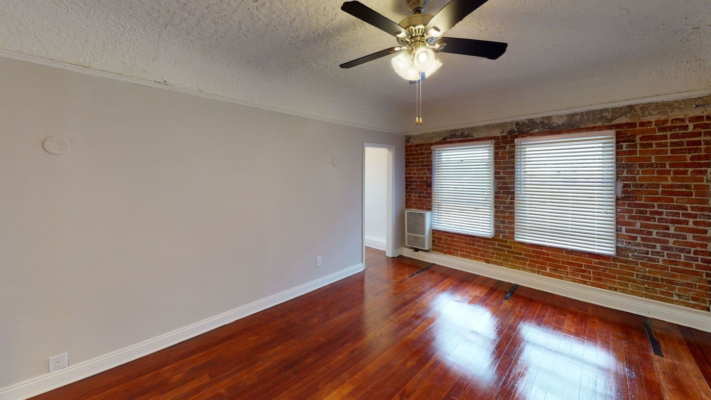 Living room with exposed brick wall, windows, wooden floor, and ceiling fan.