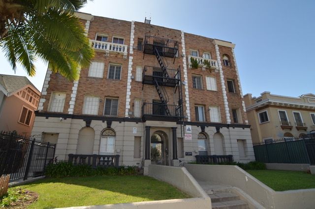 Brick apartment building with white trim, black fire escape, and grassy lawn.