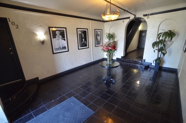 Entryway of a building with black tile floors, framed photos, and a vase of flowers.