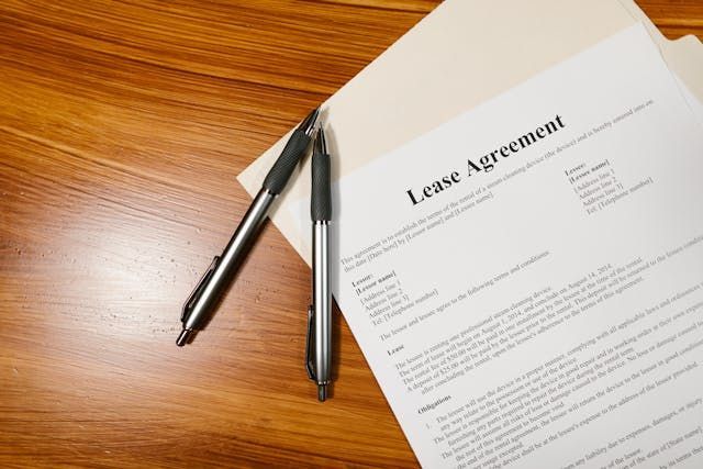 a-lease-agreement-document-on-a-wooden-surface-partially-inside-a-folder-with-two-pens-placed-beside-it