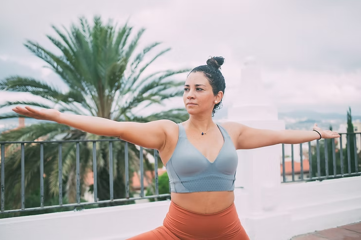 Woman in athletic wear doing yoga pose outdoors, arms outstretched.