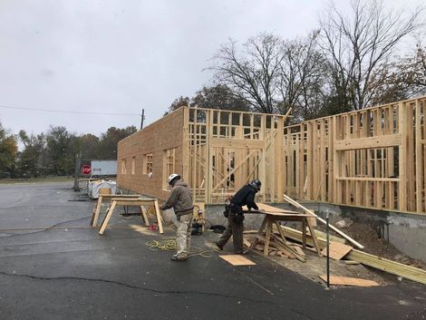 Two construction workers are working on a building in a parking lot.