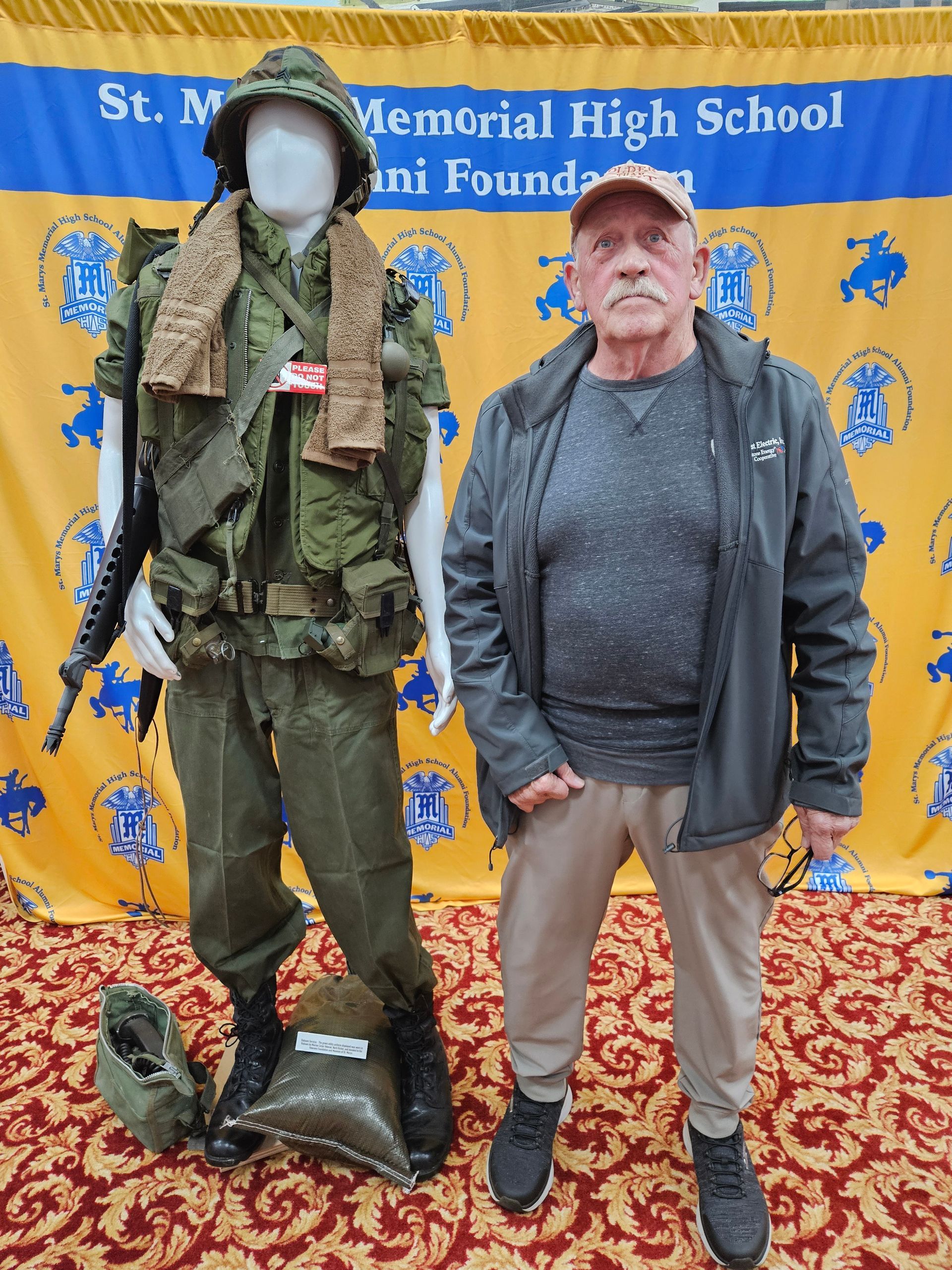 Man standing next to a mannequin dressed in Vietnam War-era military uniform; banner in background.