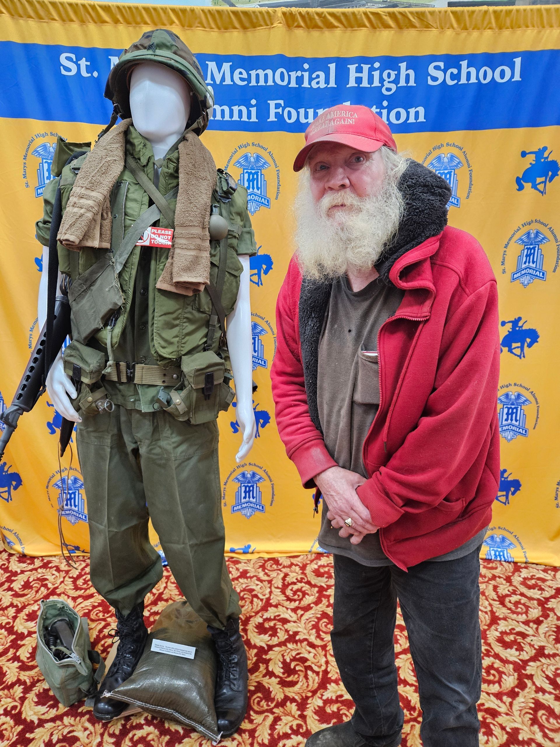 Man stands by a Vietnam War uniform display; red jacket, white beard.