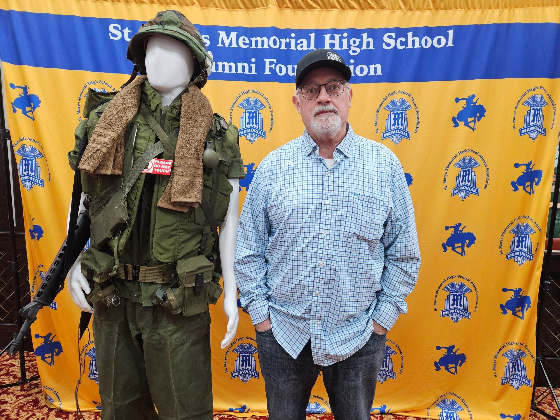 Man stands next to a mannequin wearing a military uniform. Background is a school banner.