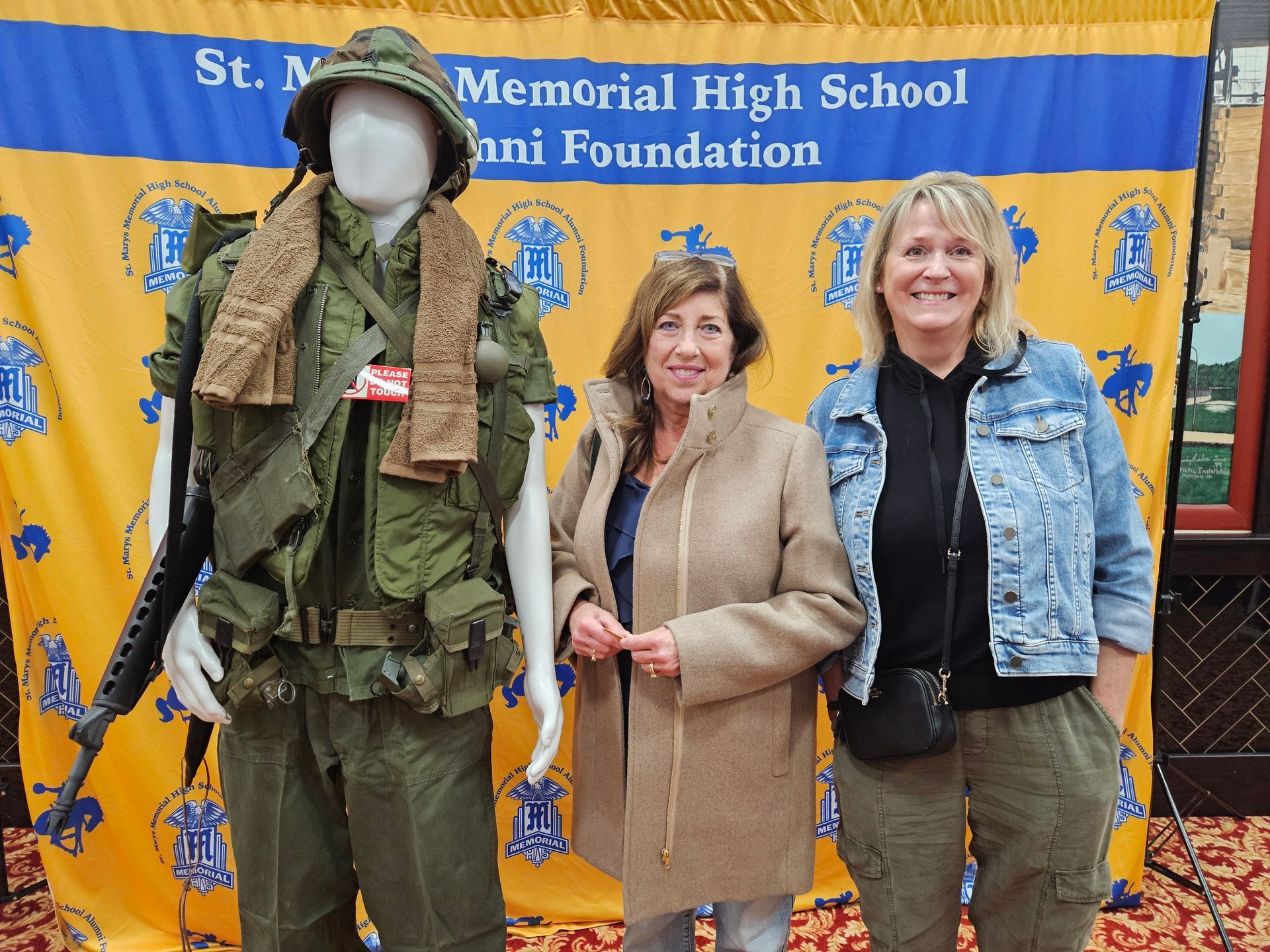 Two women stand near a mannequin wearing a Vietnam-era military uniform in front of a banner.