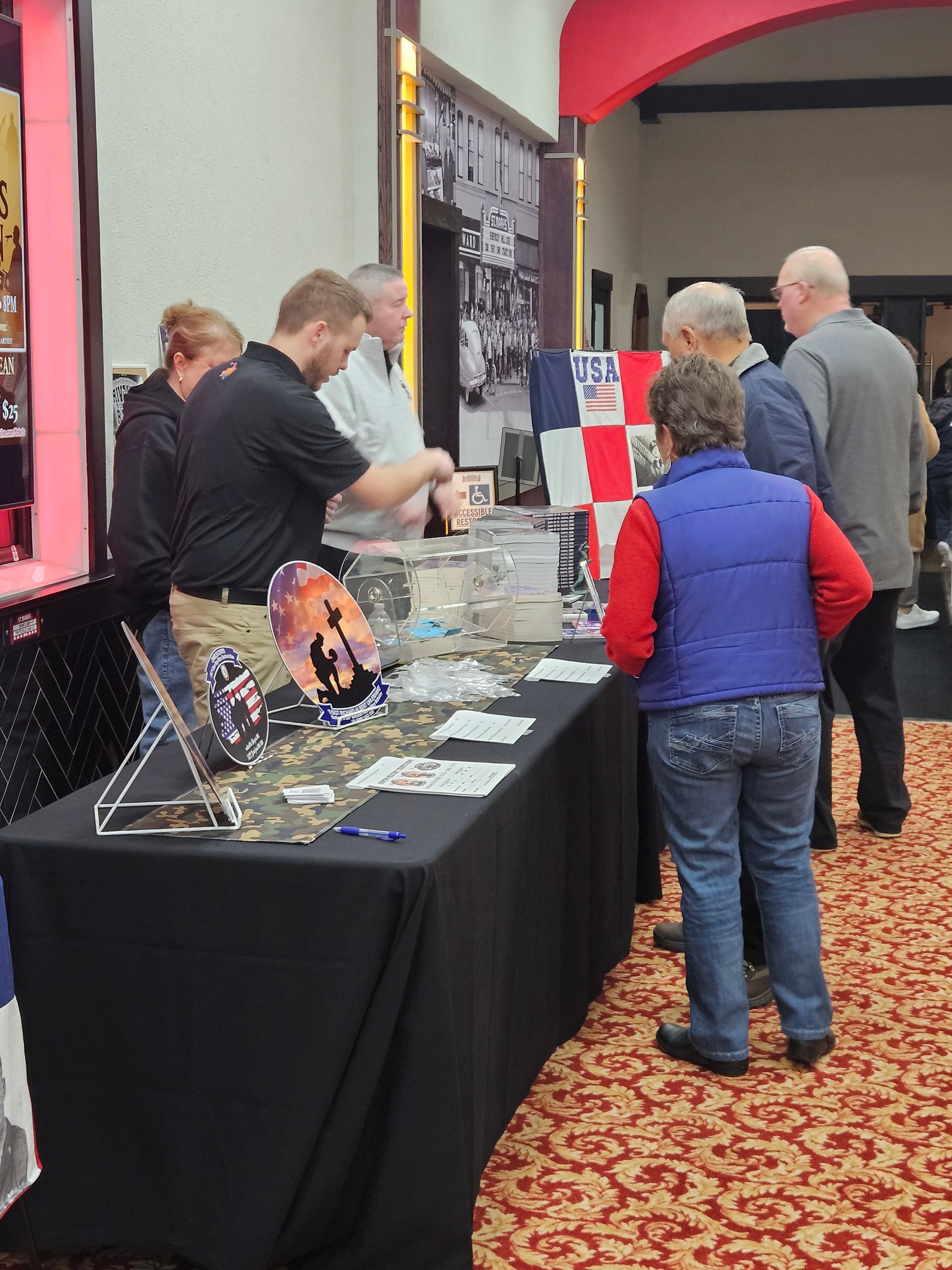 People at a booth with a table covered in promotional material. Man in black shirt interacts with visitors.