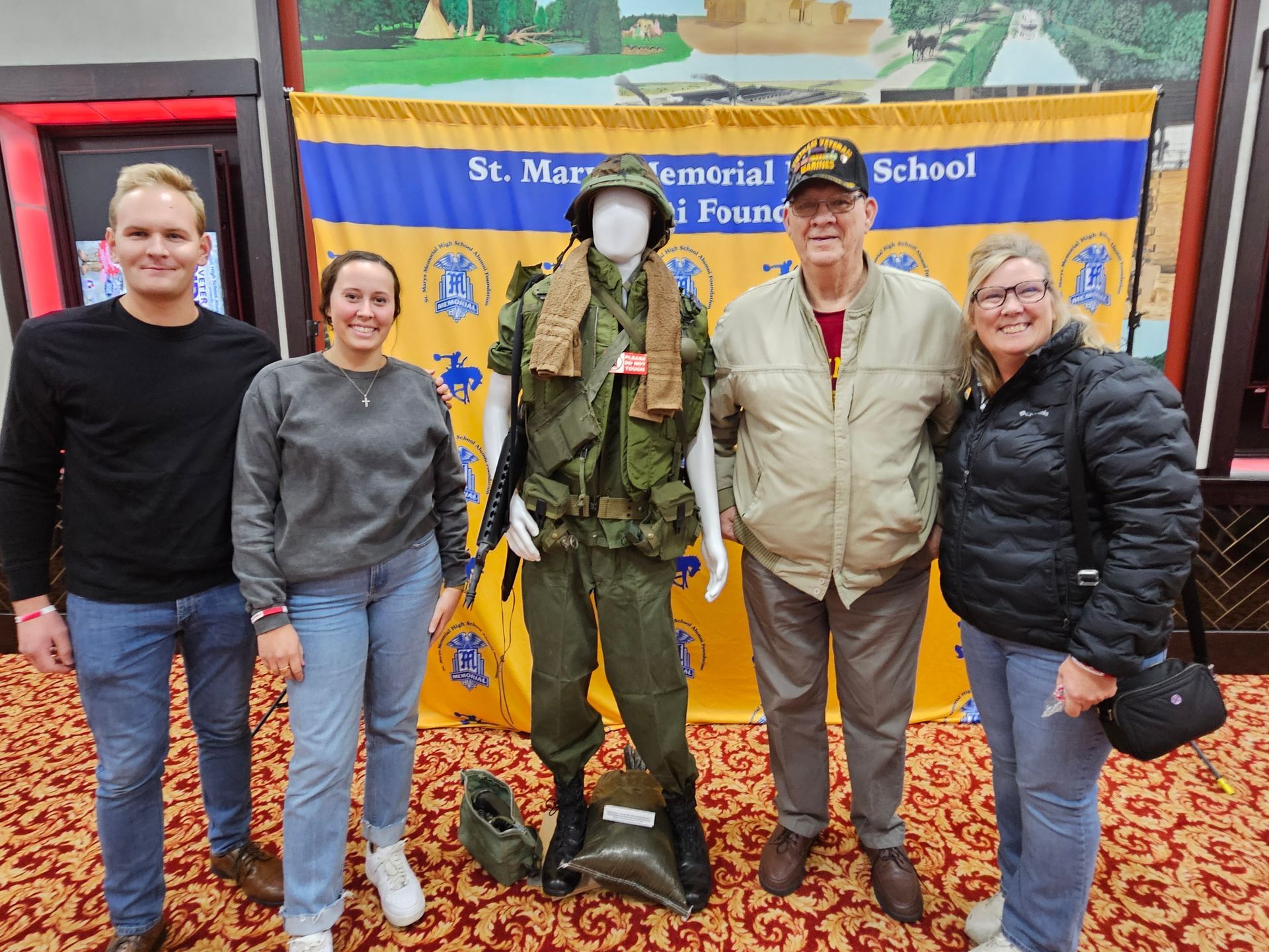 Five people stand with a military uniform display; a banner reads 