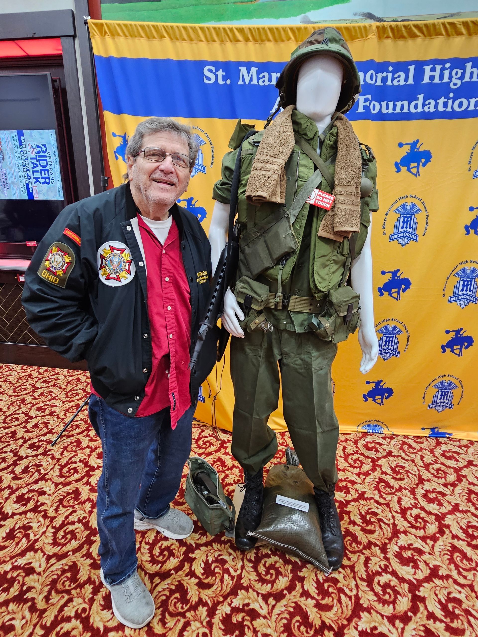 Man beside a mannequin in military uniform, standing in front of a banner.