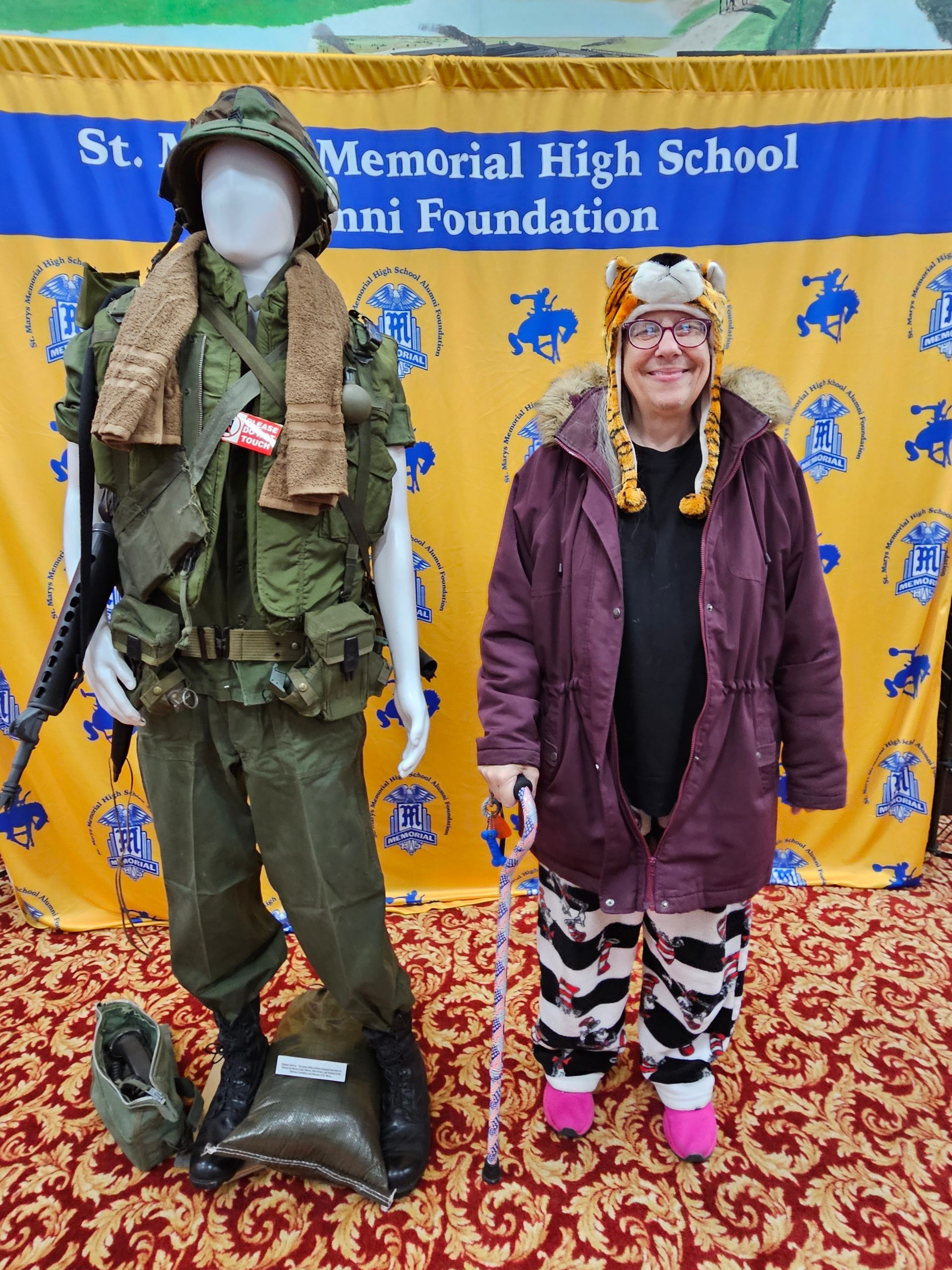 Person stands next to a mannequin in a military uniform. Person wears winter coat and tiger hat.