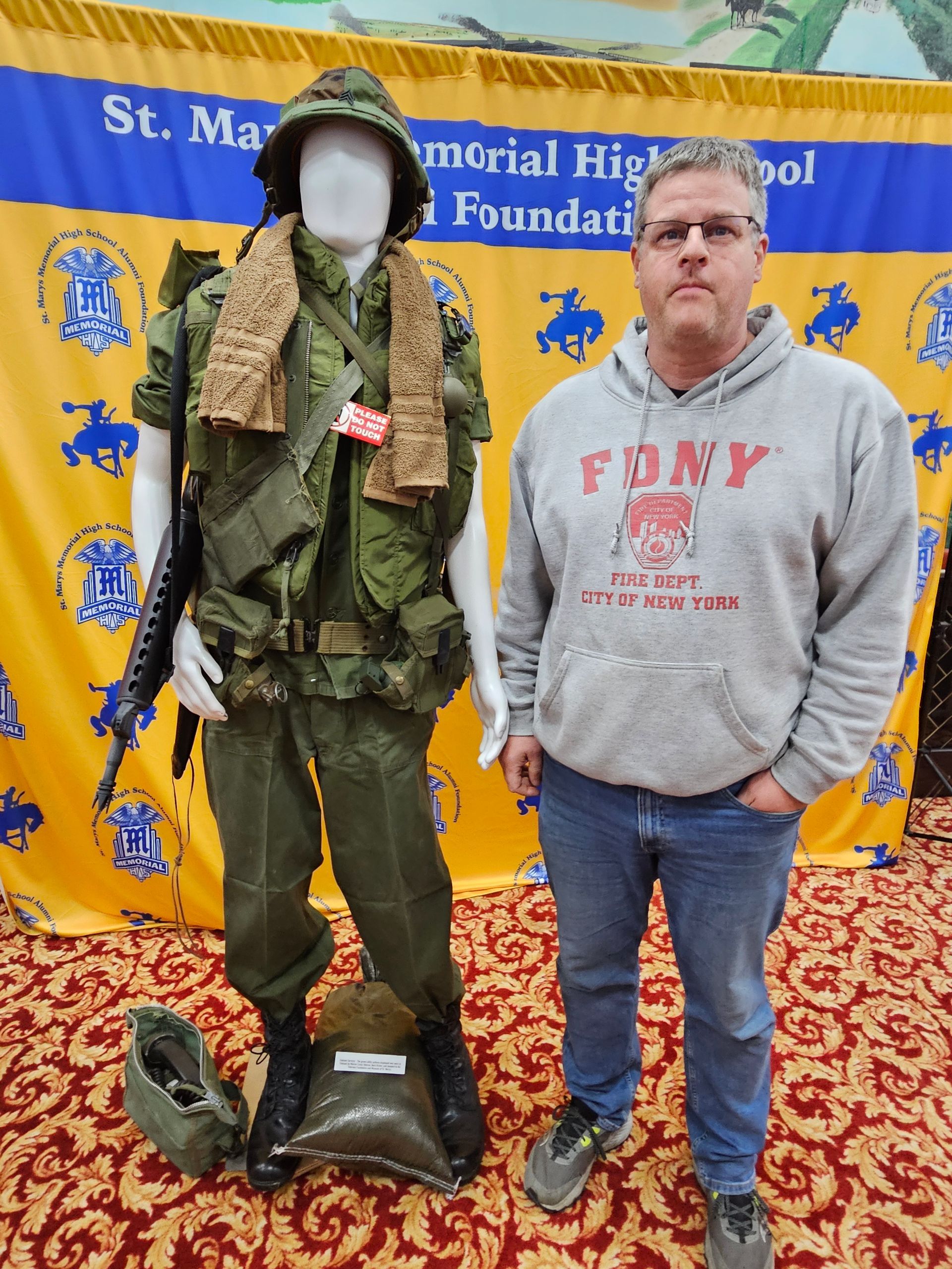 Man stands next to a Vietnam War uniform display at St. Mary's High School.