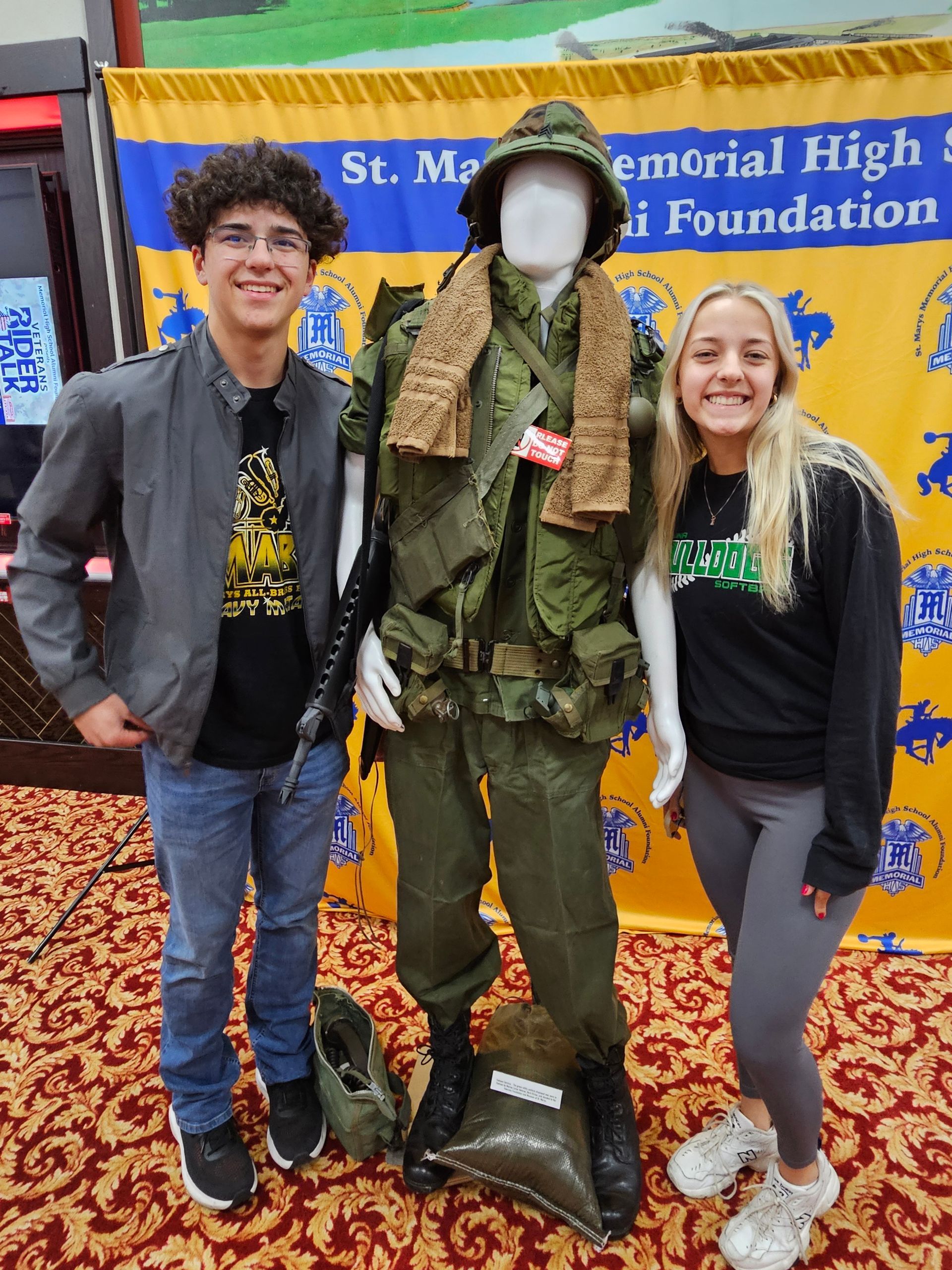 Two people pose with military uniform display at event.