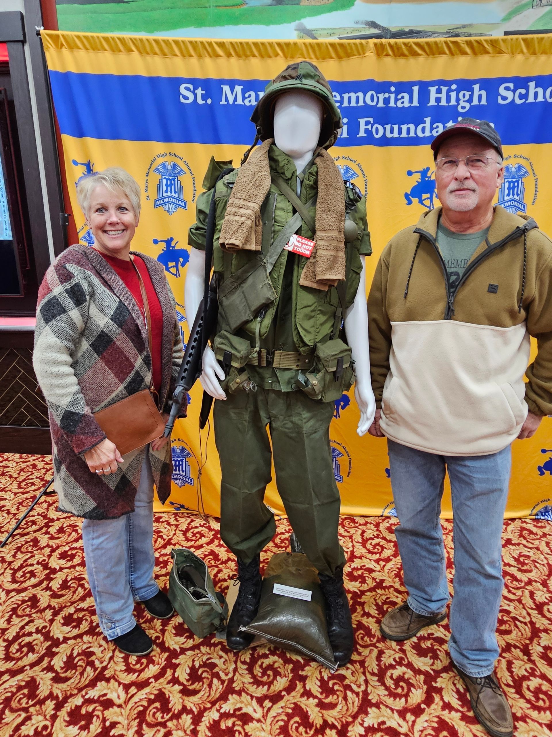 Two people stand next to a mannequin dressed in a military uniform.