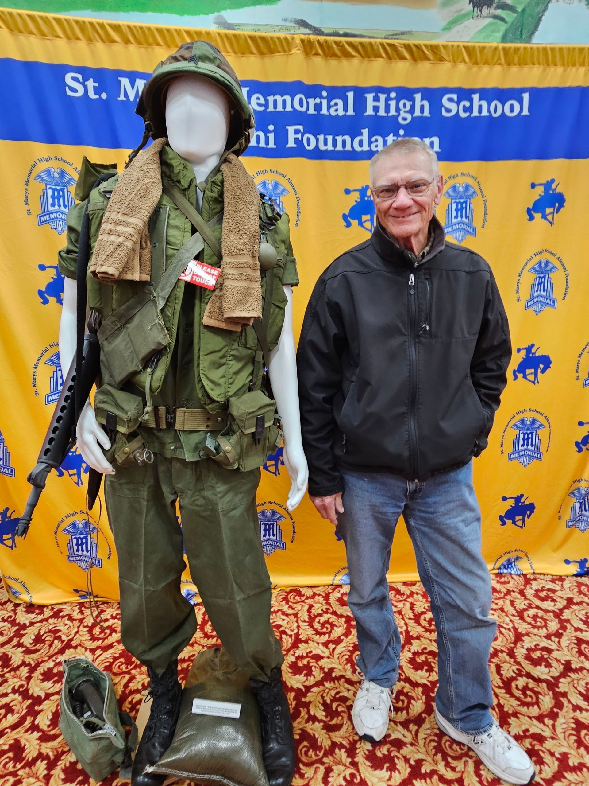 Man stands next to a Vietnam War uniform display. The man wears a black jacket and jeans.