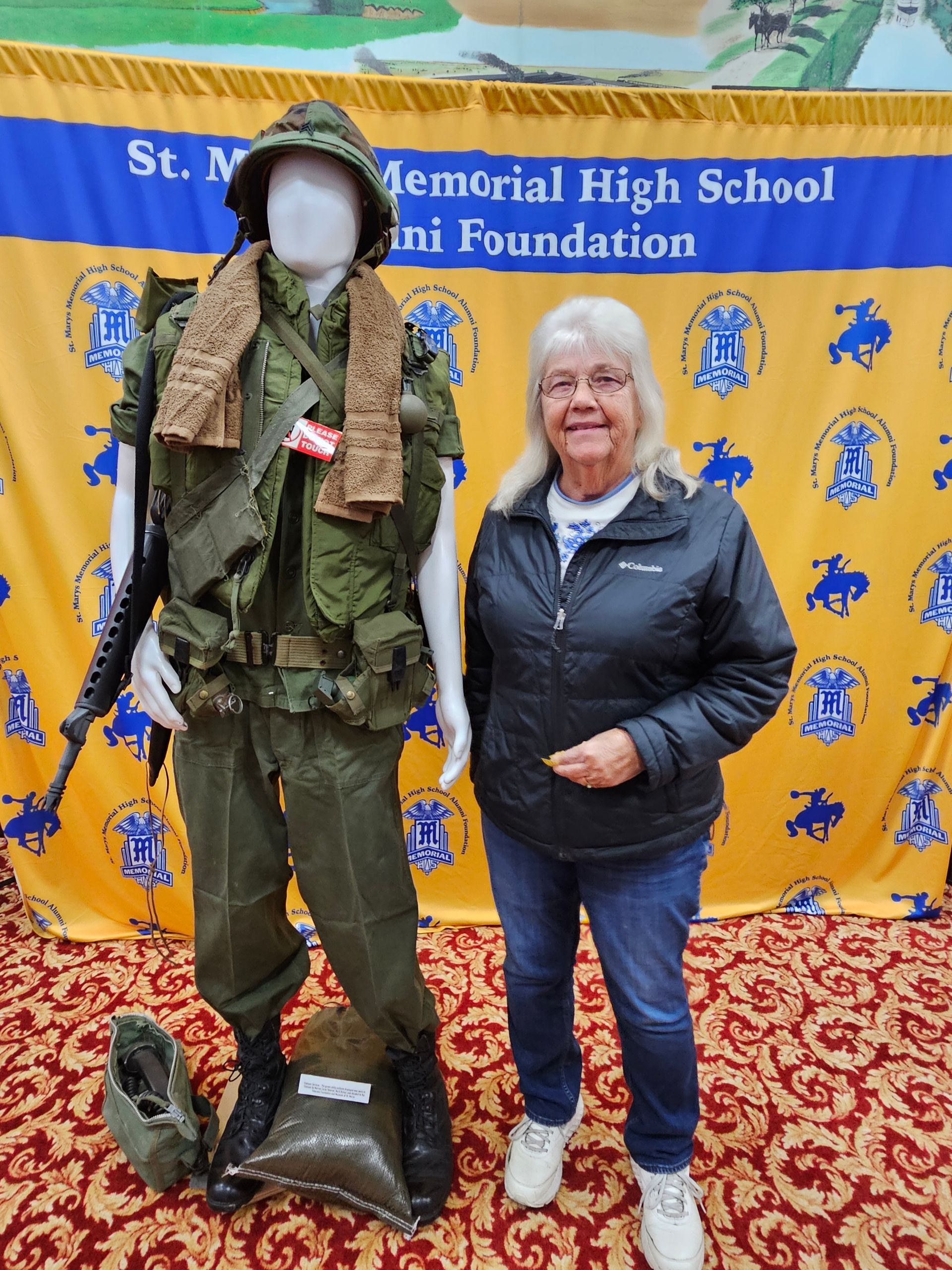 Woman standing next to a mannequin dressed in Vietnam War-era military gear. Behind them, a banner.