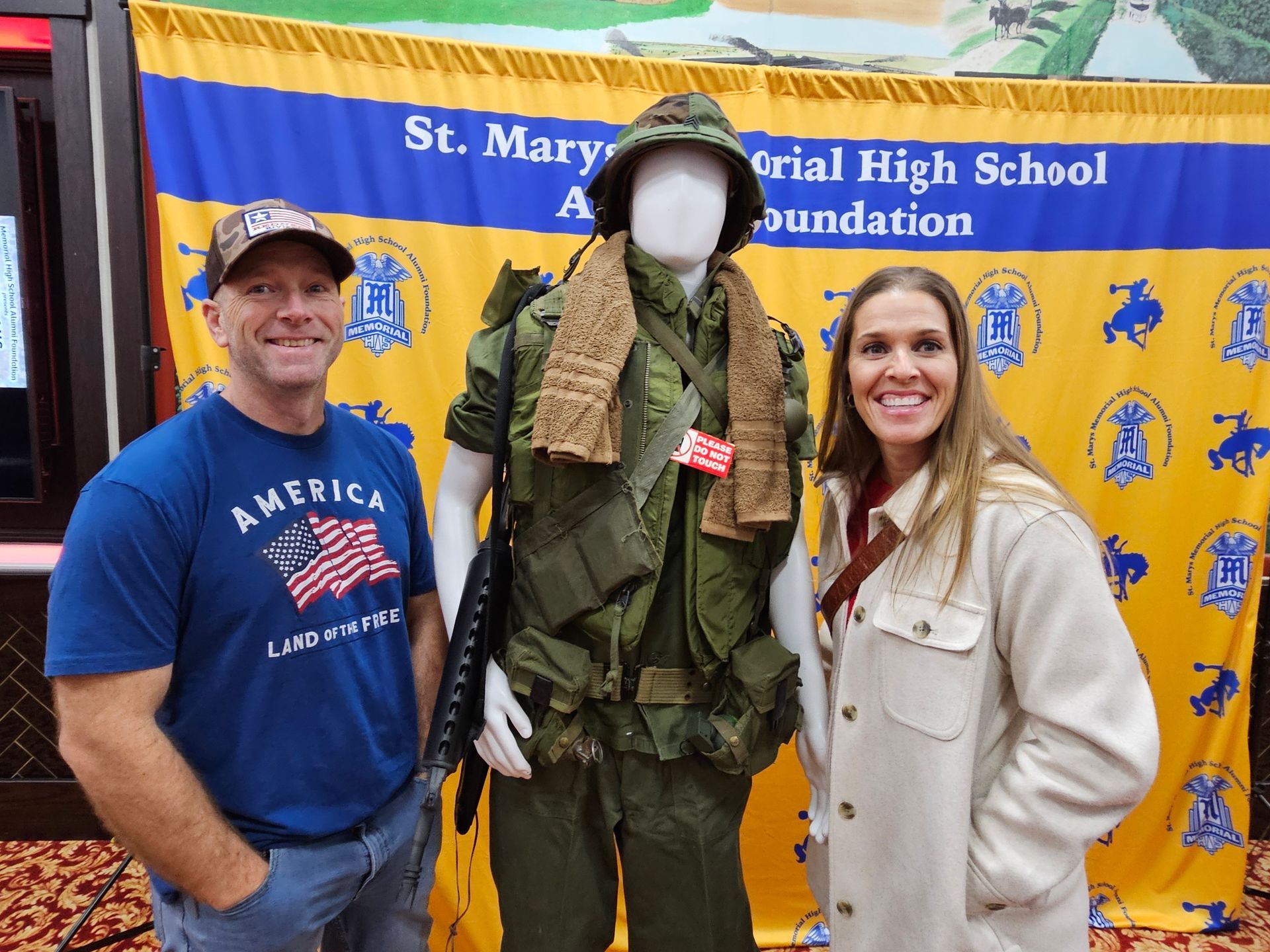 Man and woman posing with mannequin in military uniform, banner behind.