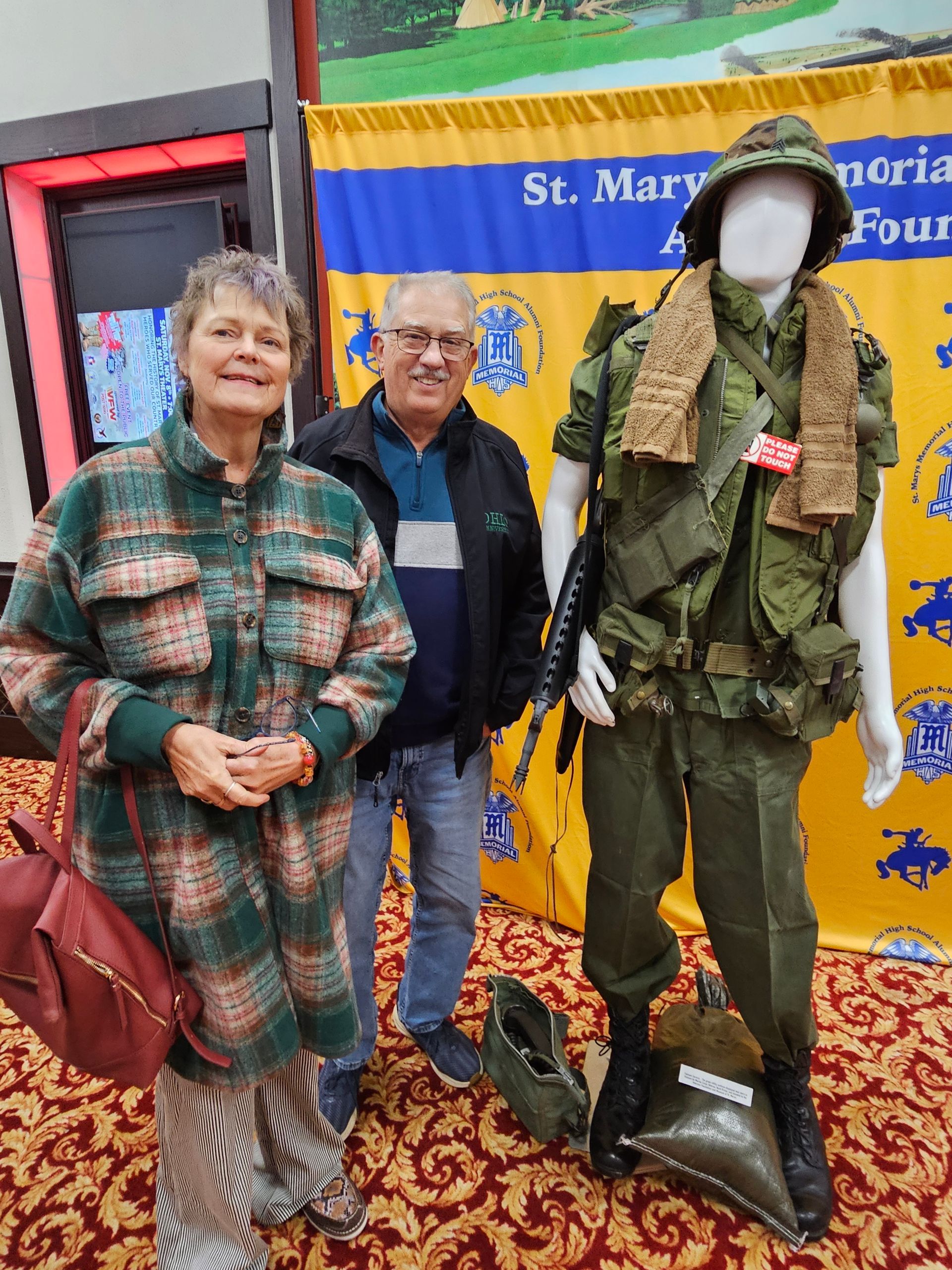 Couple poses beside military uniform display at event.