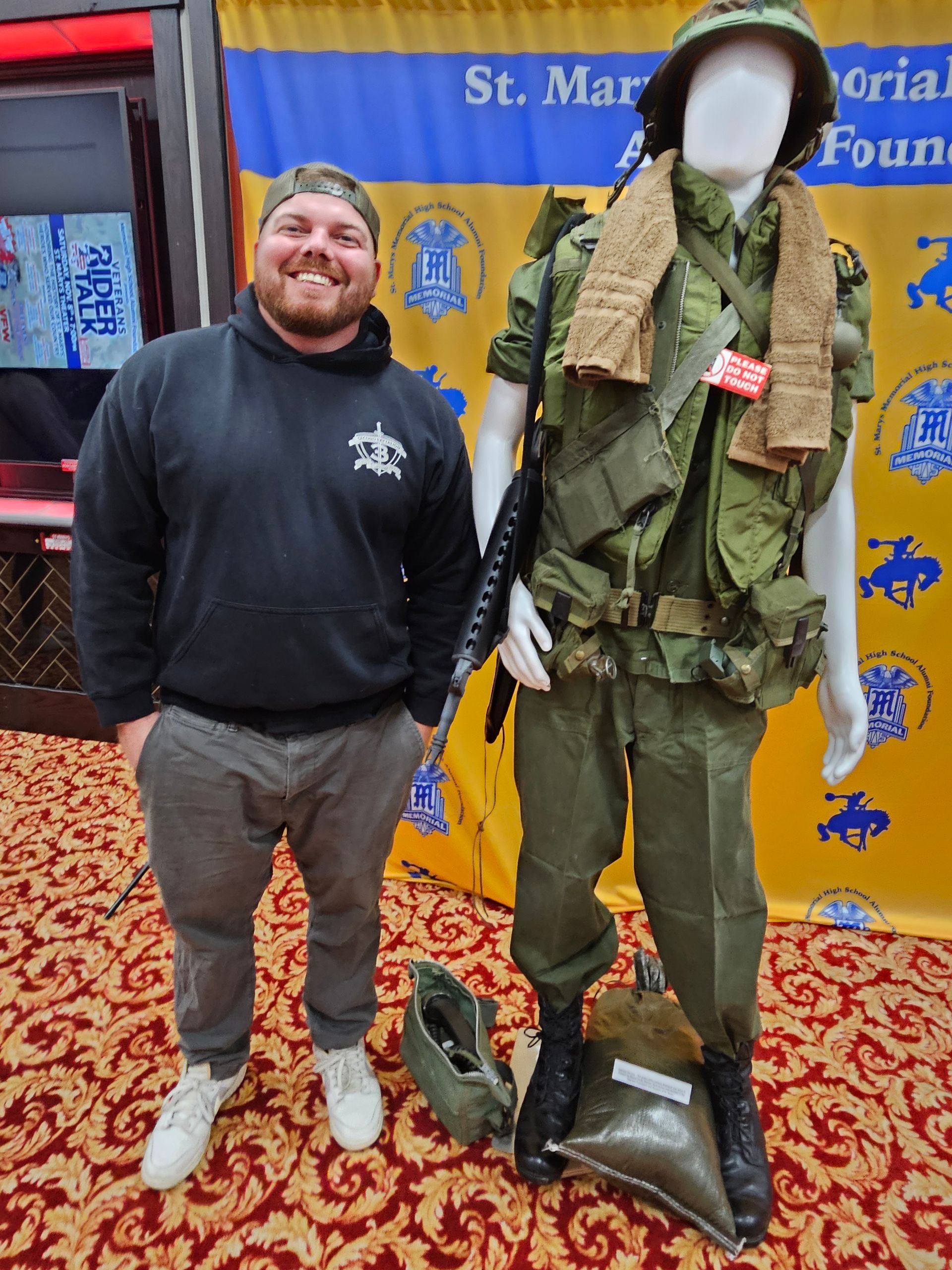 Man standing next to a mannequin in a military uniform. Background with banners and carpet.