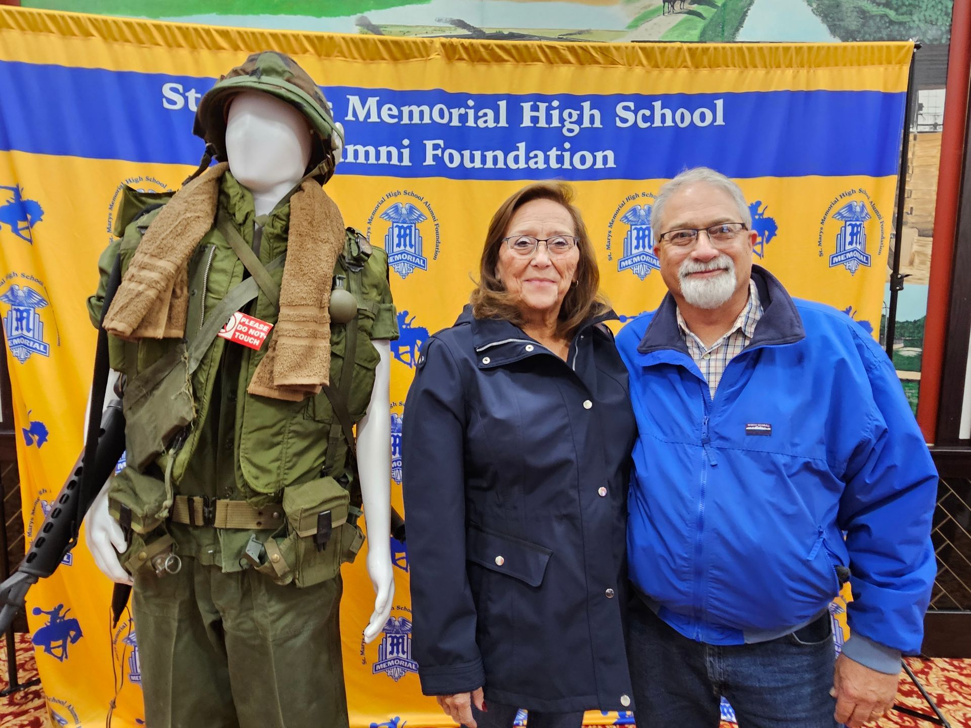 Couple standing next to a Vietnam War uniform display at a high school alumni event.