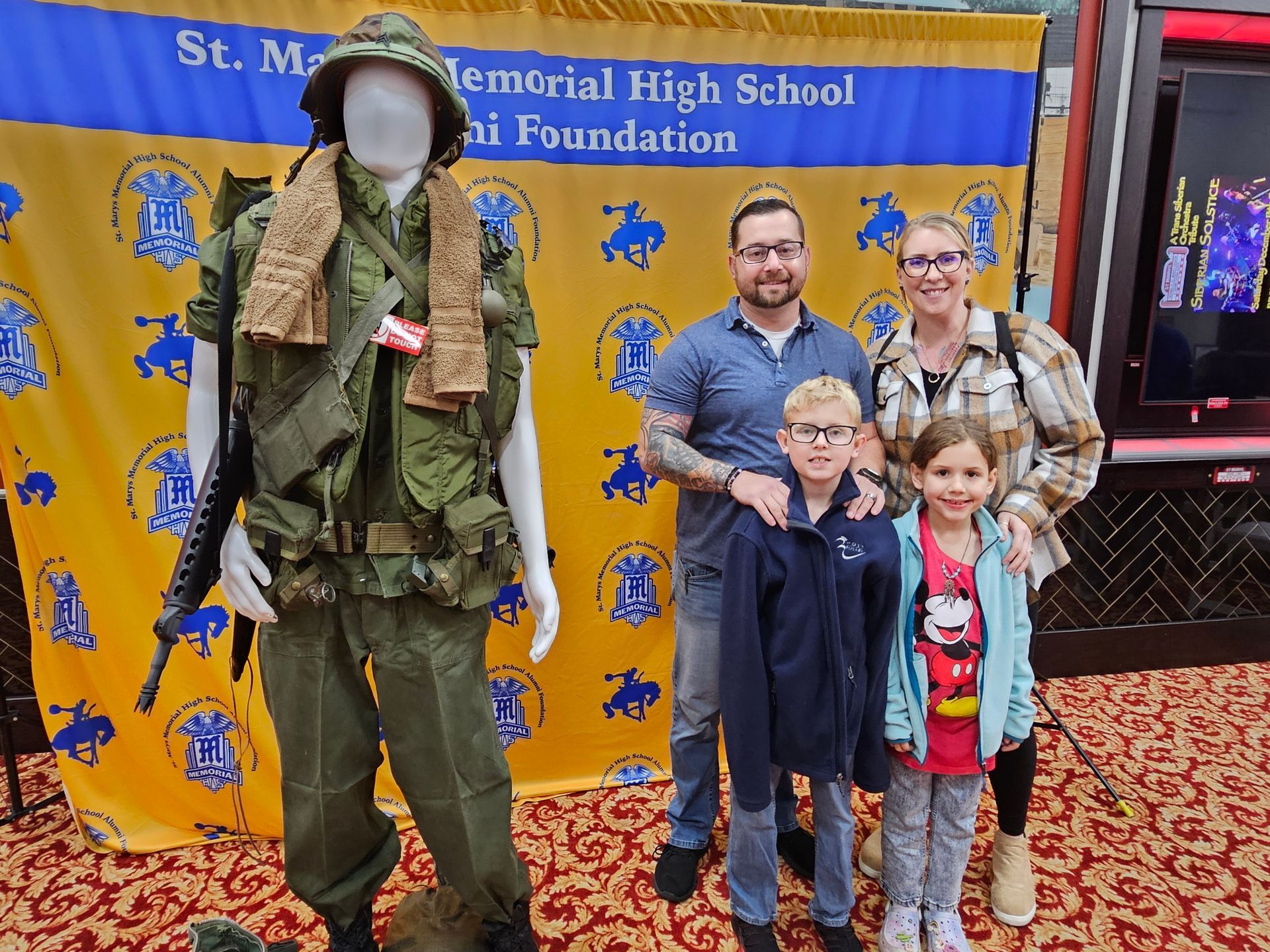 Family posing in front of a backdrop, a mannequin wearing a military uniform is to the left.