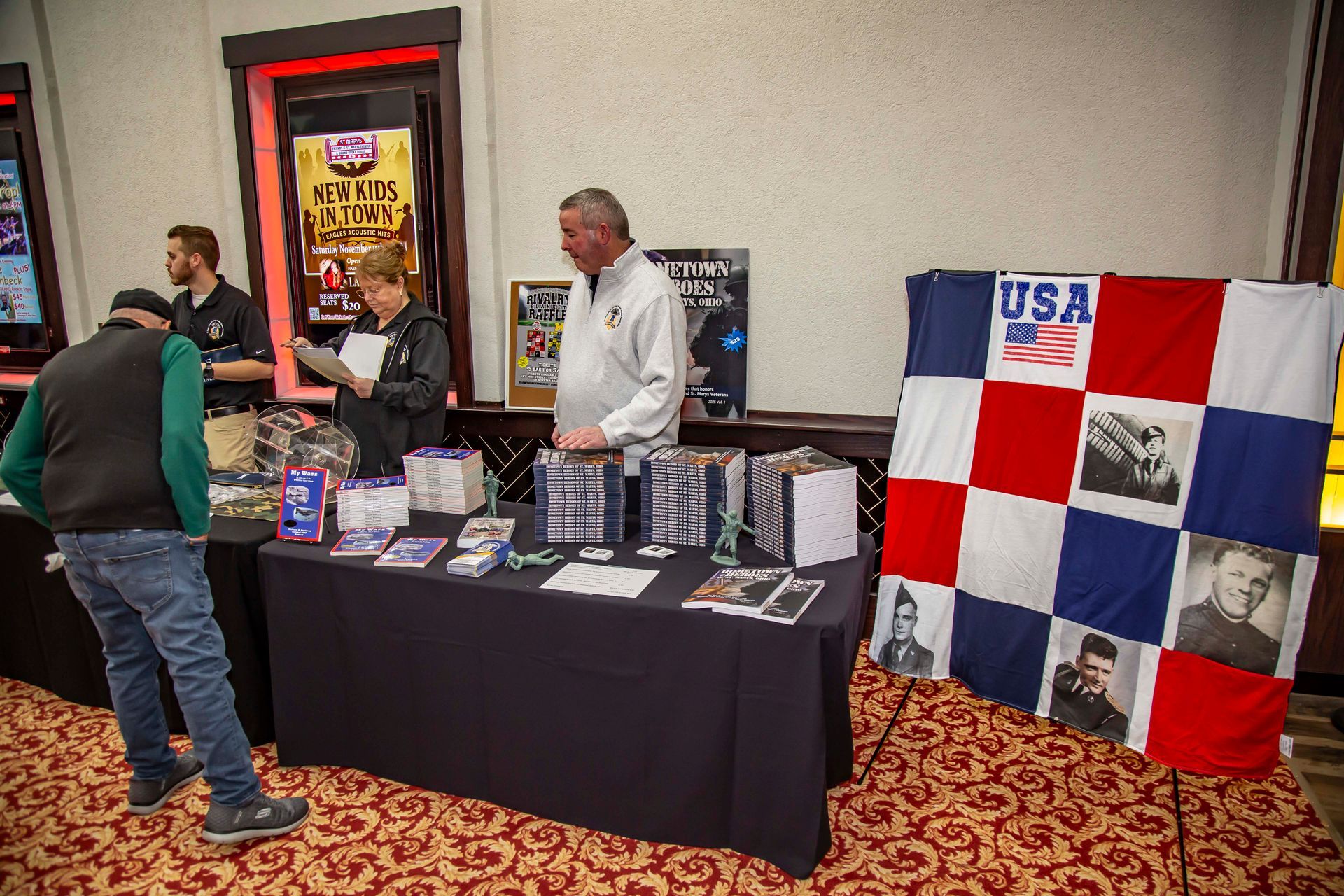 Booth with merchandise, people, and a USA flag at an event.