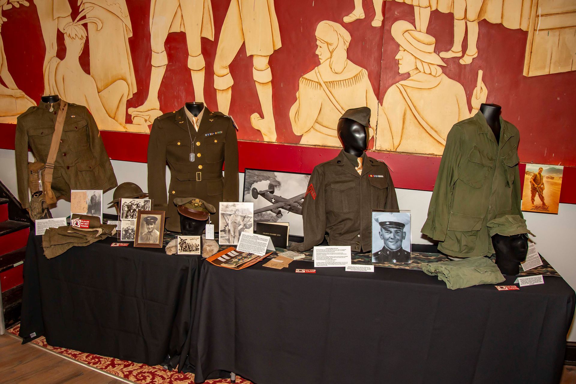 Display of military uniforms and artifacts on a table with a mural backdrop.