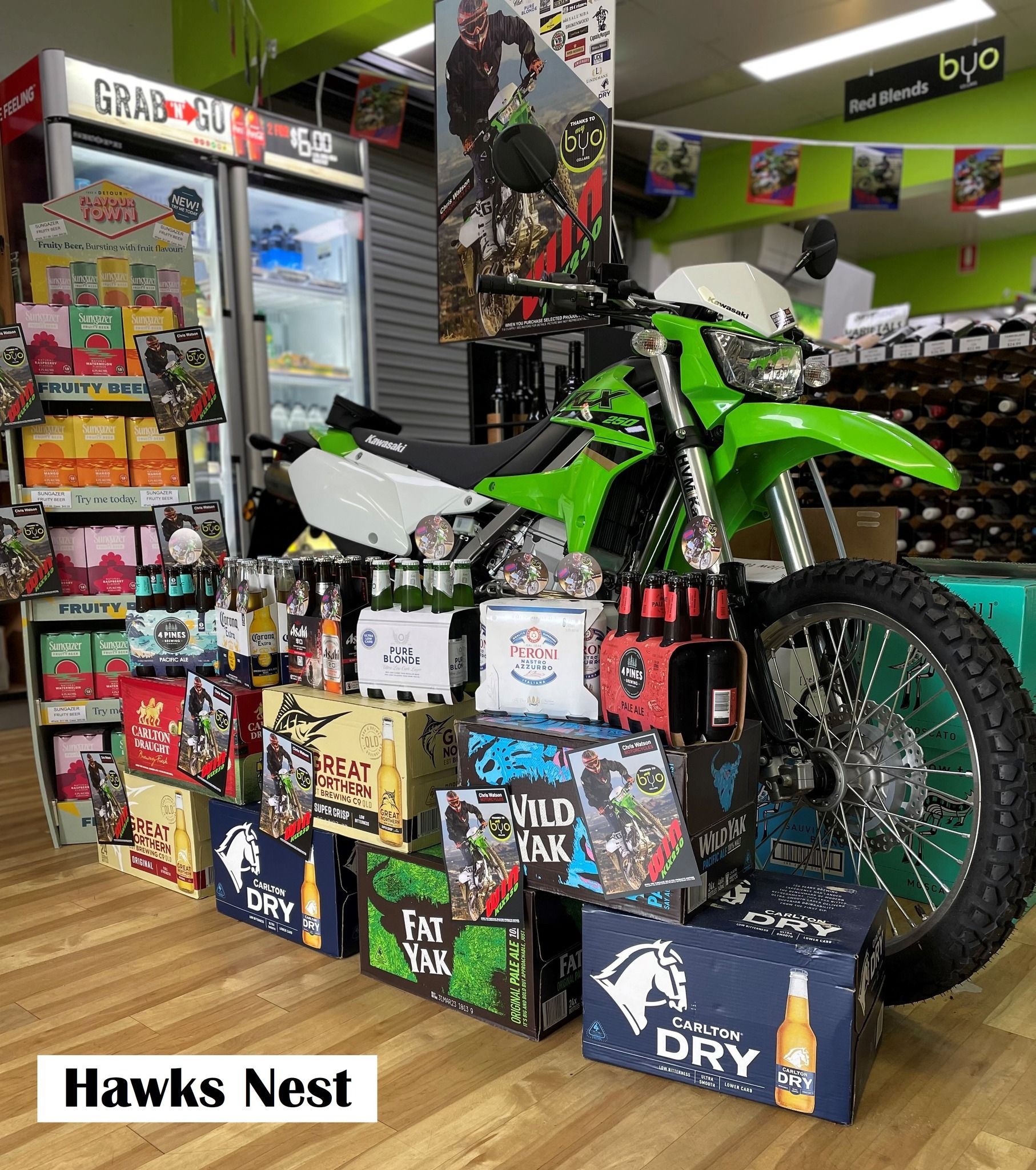 Green motorcycle display at Hawks Nest, surrounded by beer cartons and shop displays.