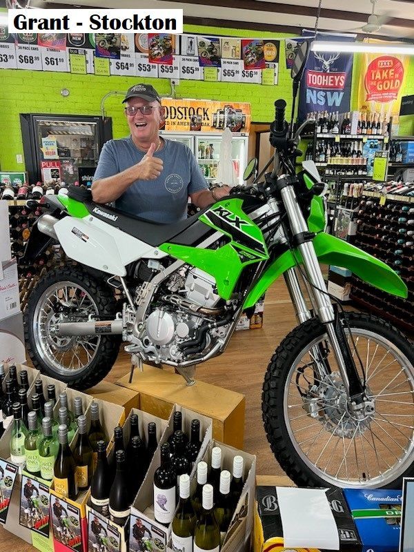 Man giving thumbs up next to a green Kawasaki dual-sport motorcycle inside a store.