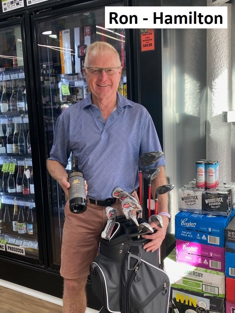 Man in front of beverage cooler, holding golf clubs and a bottle, smiling.
