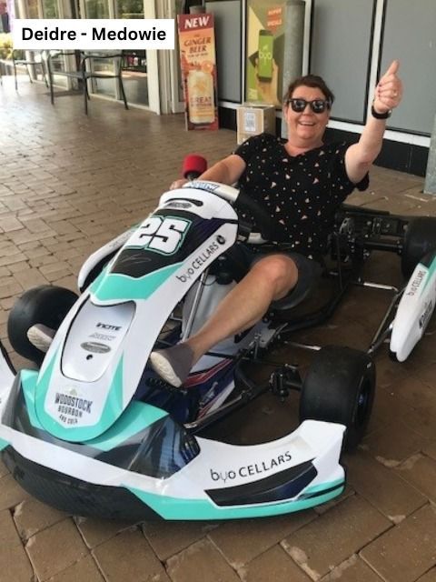 Deidre Medowie gives a thumbs-up while sitting in a go-kart with Bud Cellars branding.