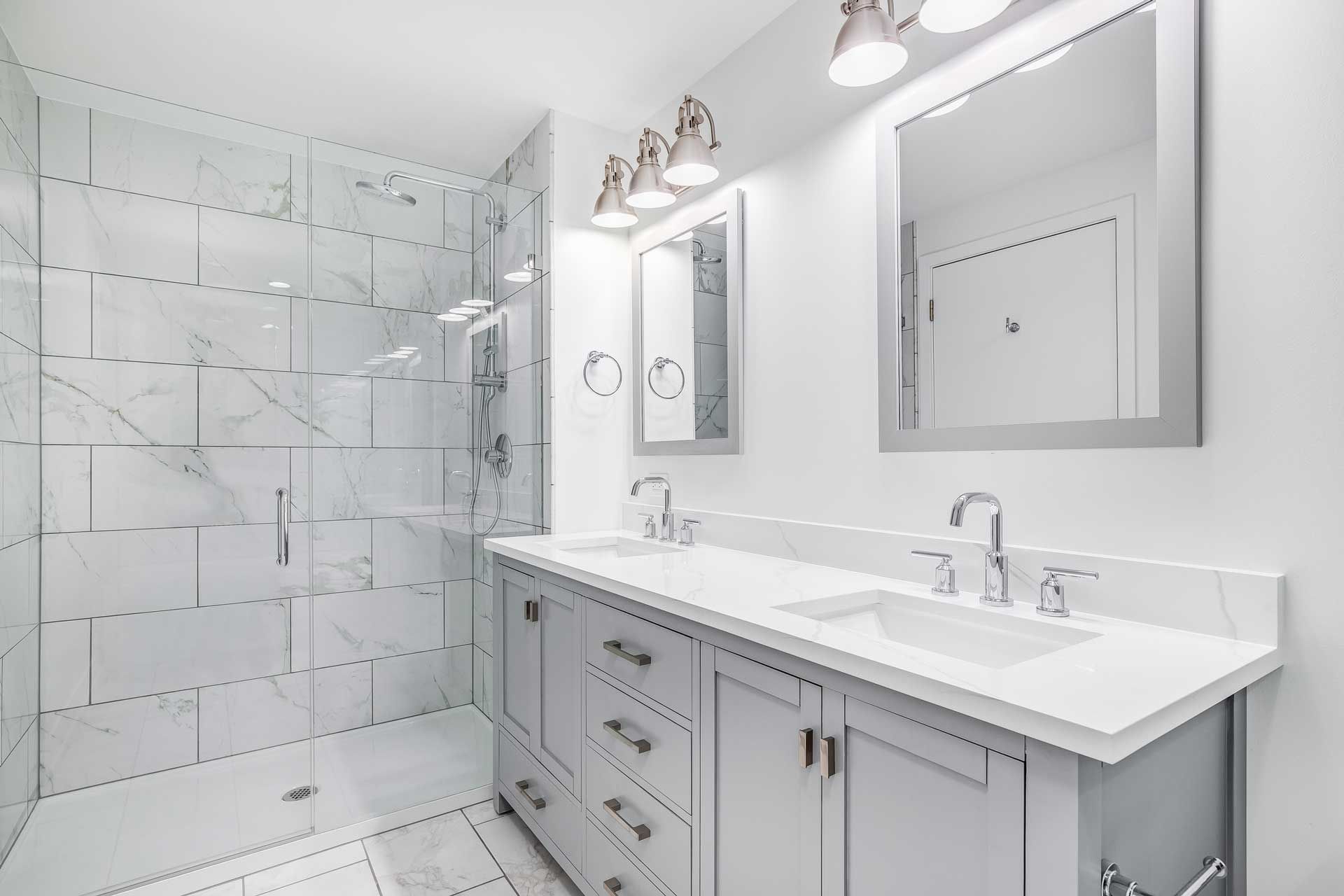 Bathroom with white marble shower, gray vanity, double sinks, and silver fixtures.