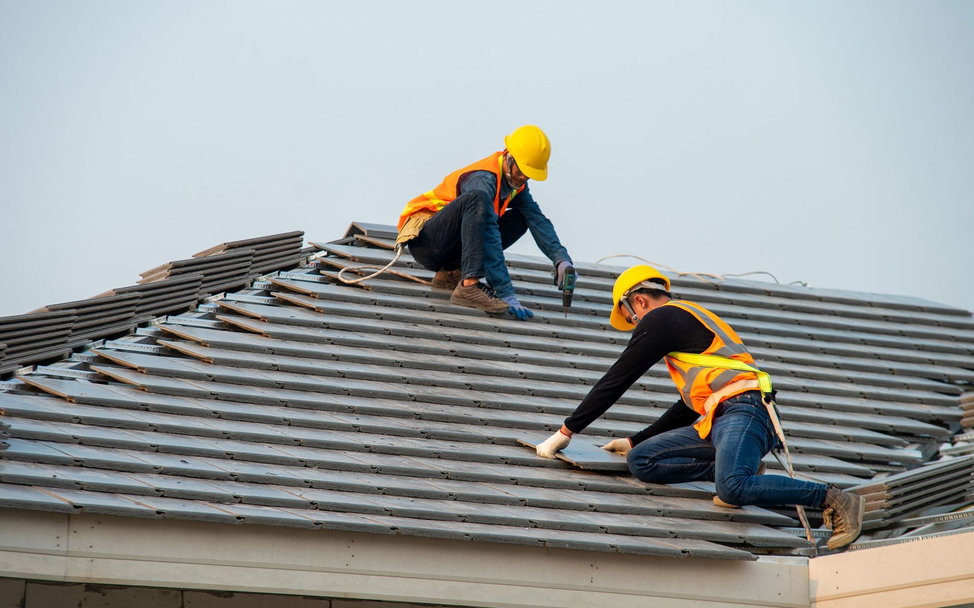 Two construction workers are working on the roof of a house.