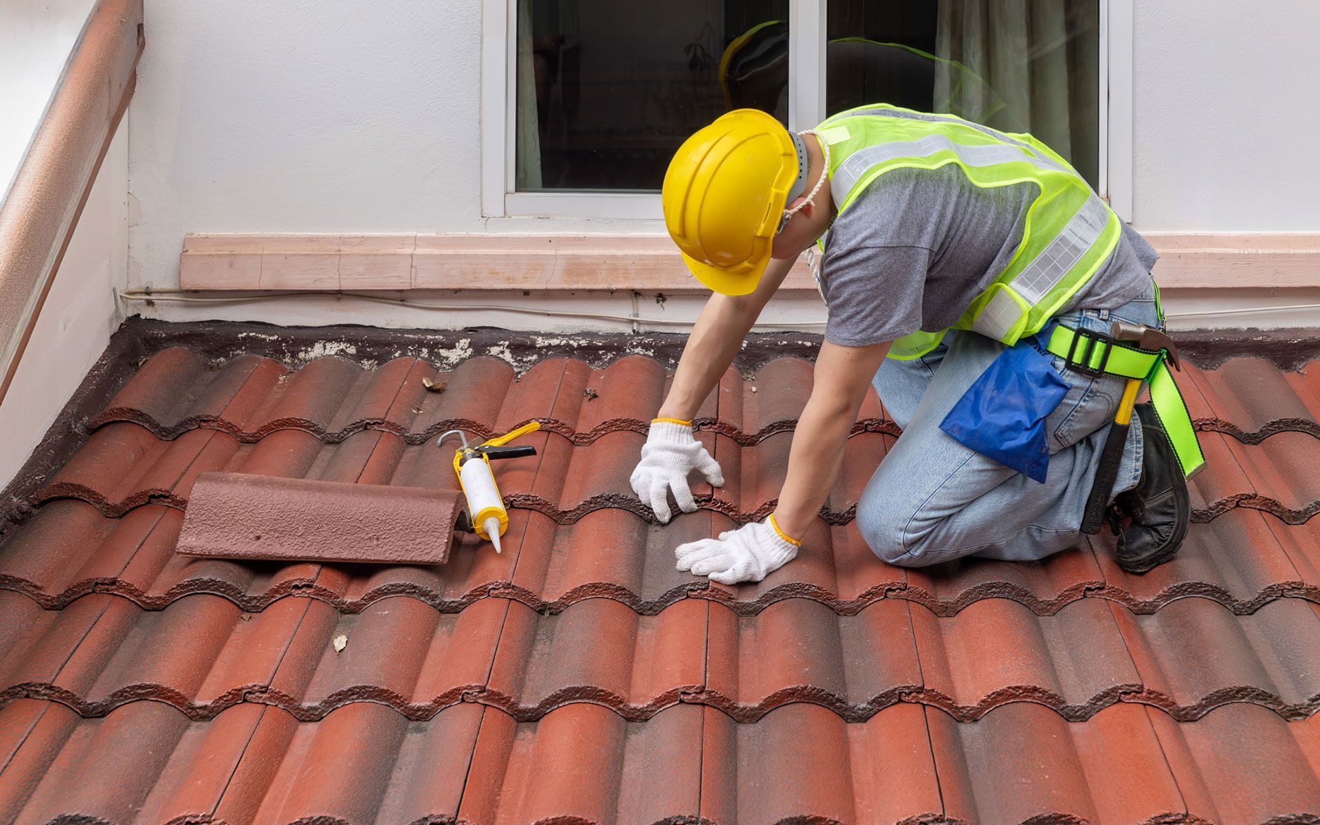 A construction worker is kneeling down on a tiled roof.