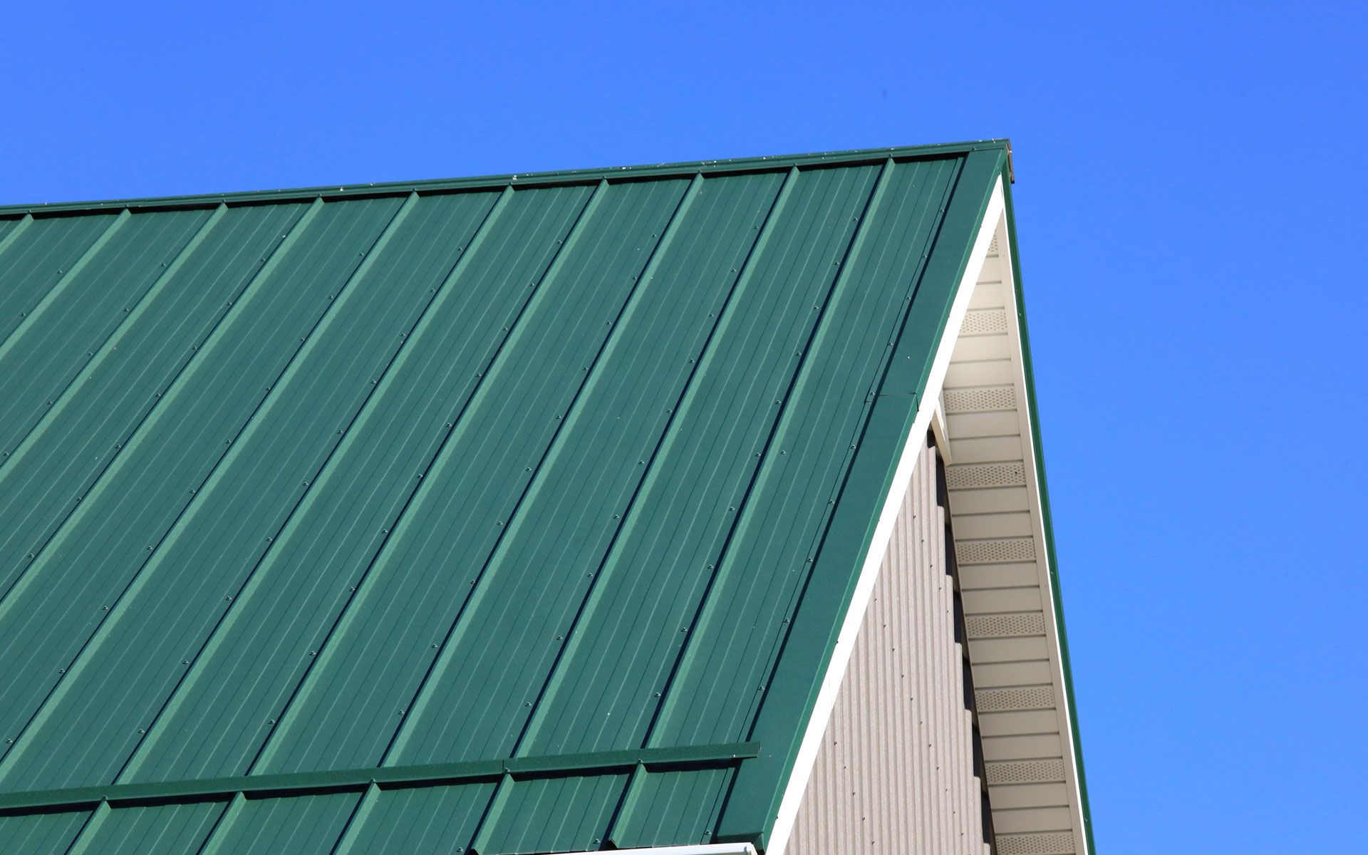 Green metal roof on a building against a clear blue sky.