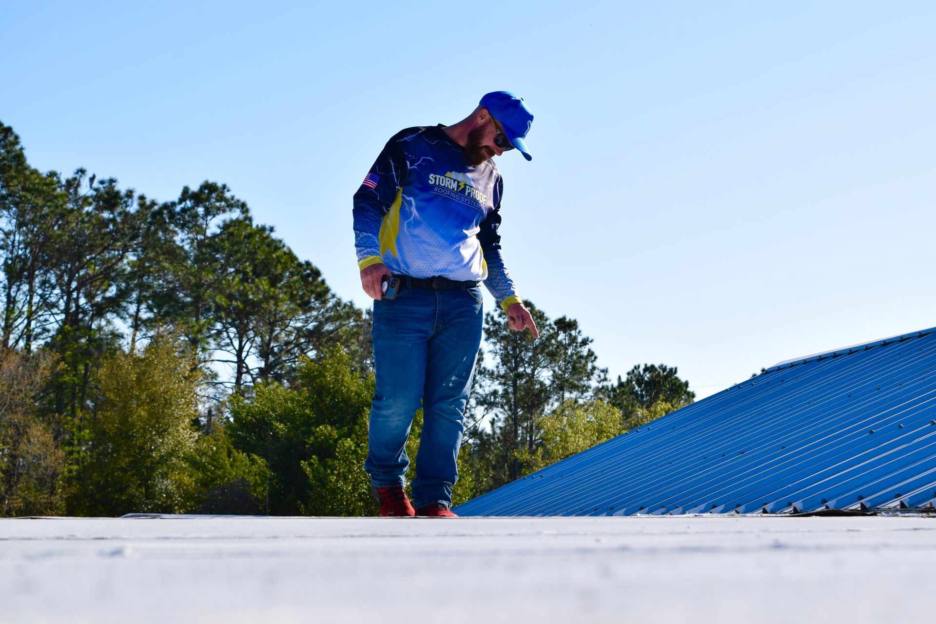 Man in blue hat and shirt inspects a white roof on a sunny day.