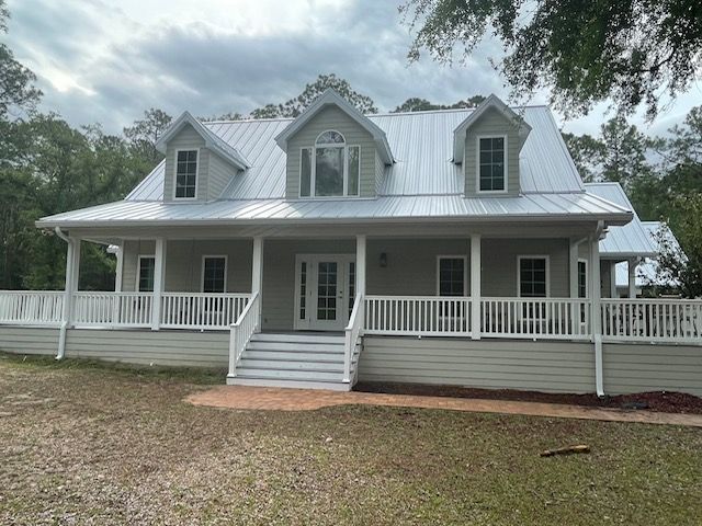 Light green house with white porch, railing, and metal roof under cloudy sky.