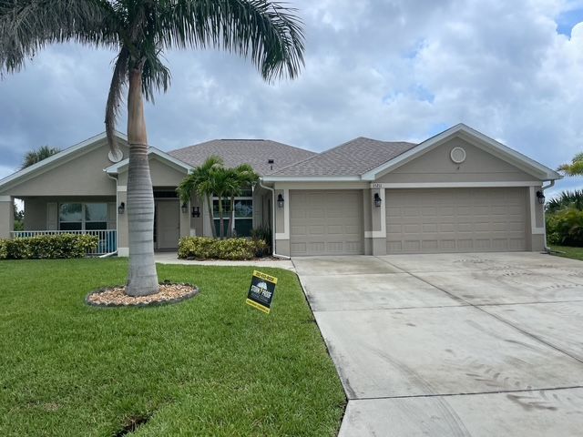 Tan ranch-style house with gray roof, two-car garage, palm tree, and green lawn under a cloudy sky.