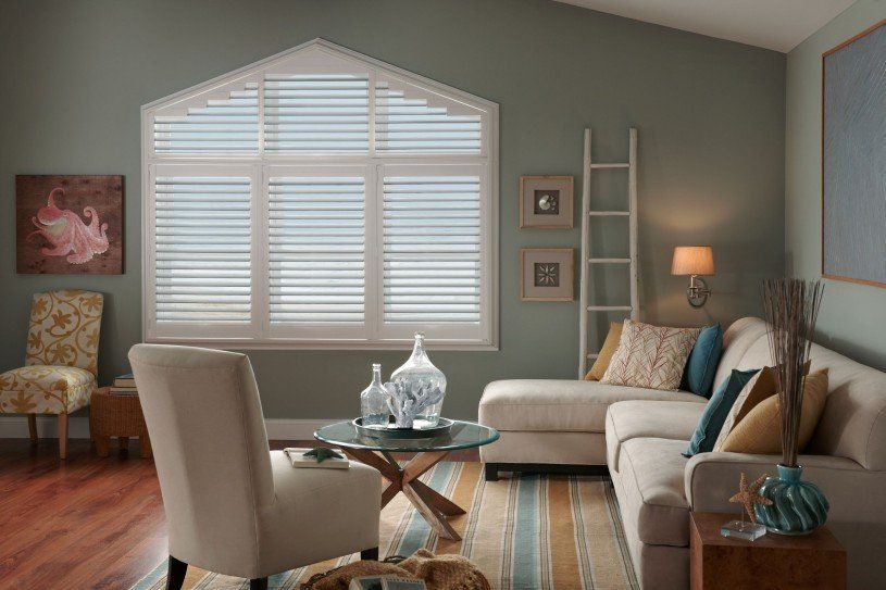 A living room with a couch , chairs , and a large window with shutters.
