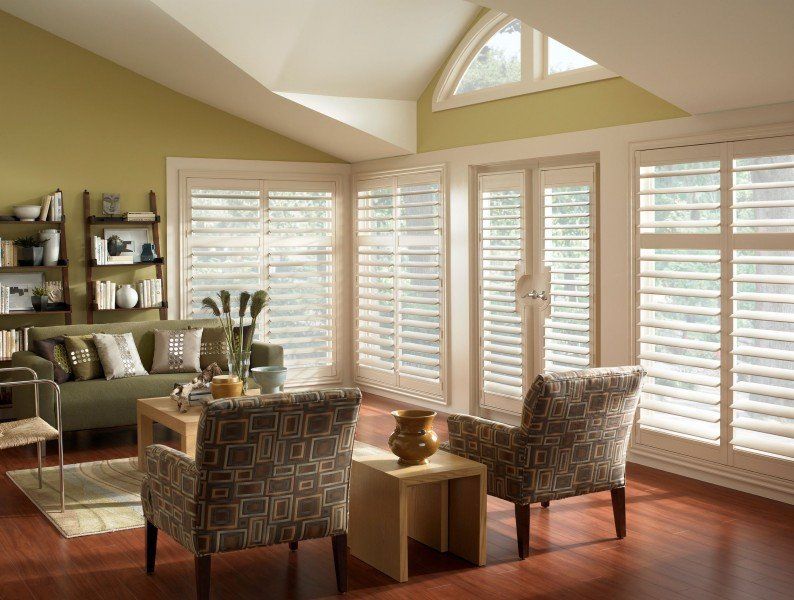 A living room with a couch and chairs and shutters on the windows