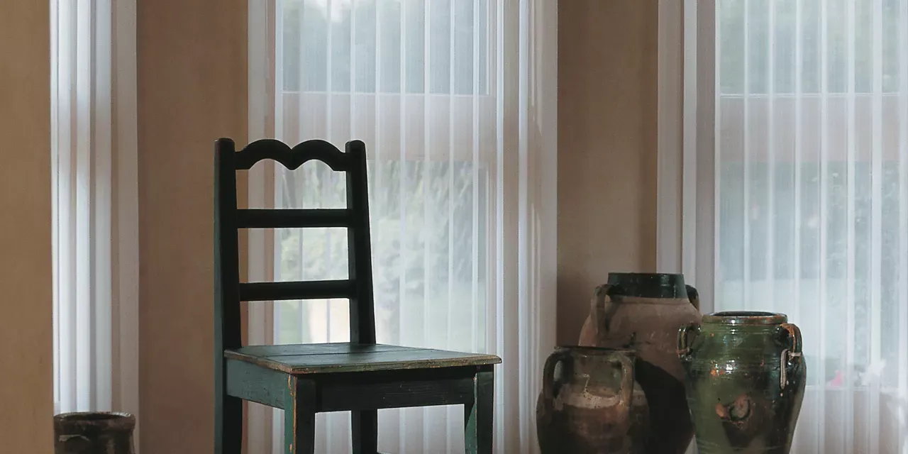 A chair and vases are sitting on a table in front of a window.