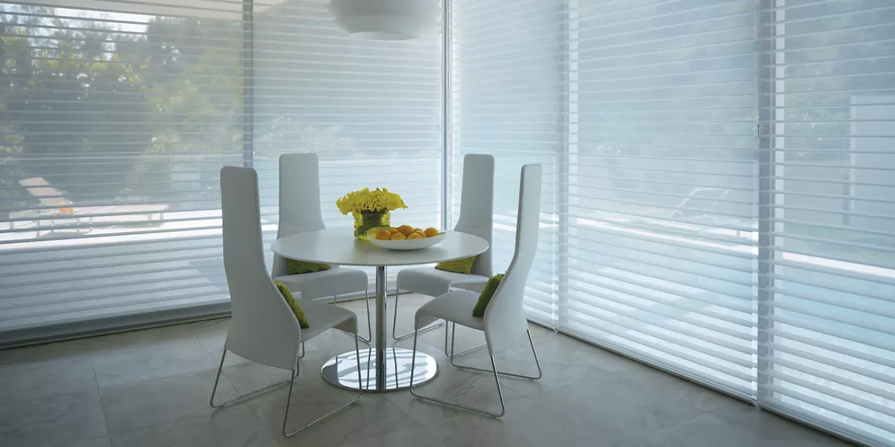 A dining room with a table and chairs in front of a window with blinds.