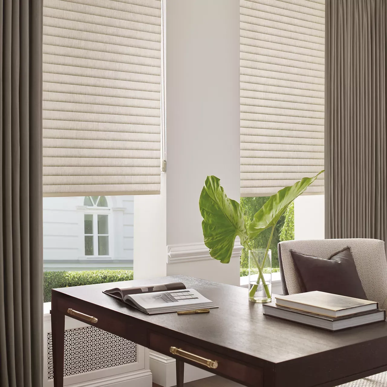 A desk with a vase of plants on it in front of a window.