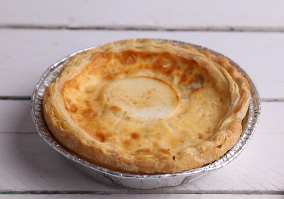 Pastel sabroso horneado en un recipiente de aluminio sobre una superficie de madera blanca.