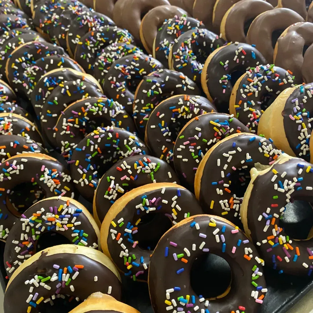 Filas de donas glaseadas con chocolate y chispitas de colores.