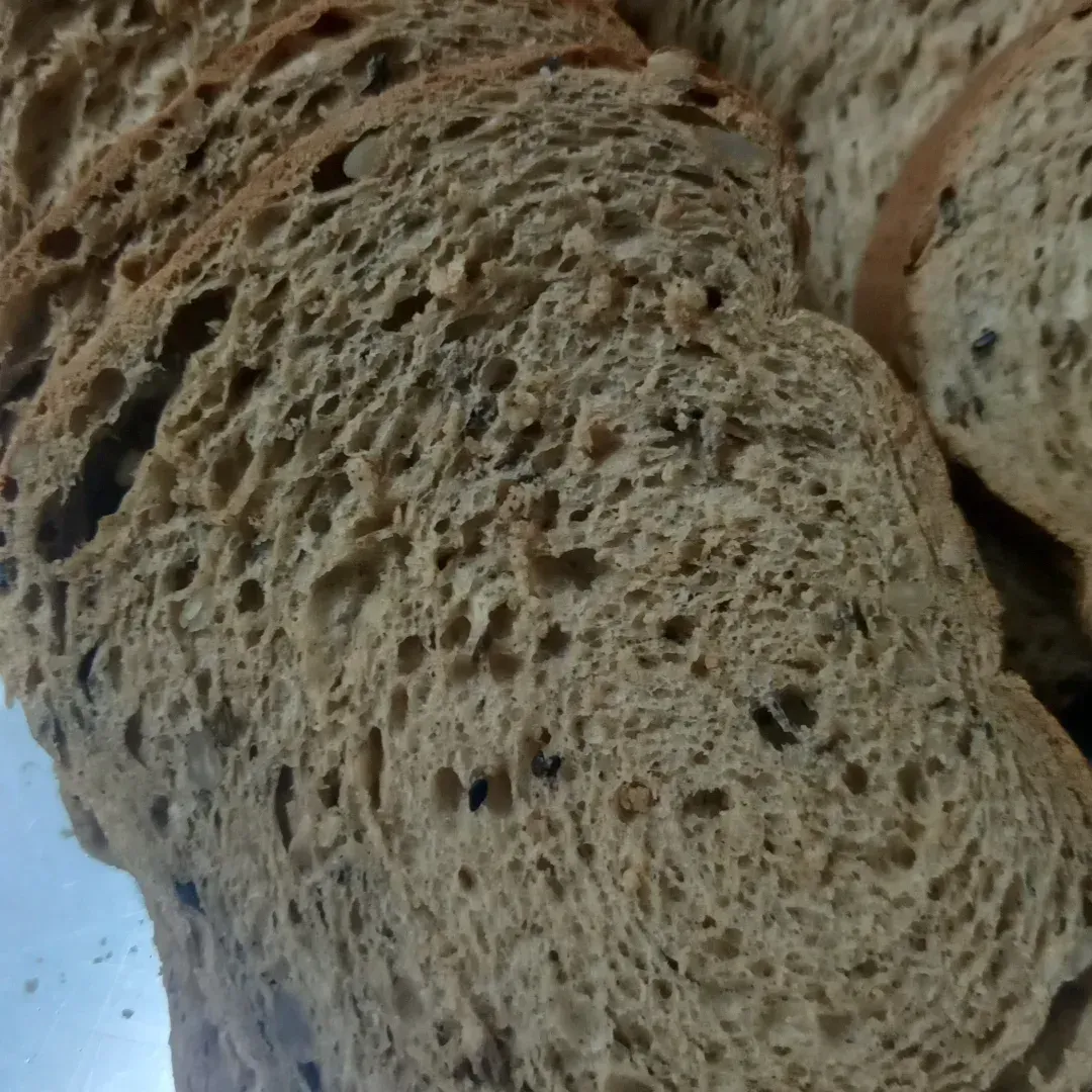 Pan integral cortado en rodajas, de cerca, con bolsas de aire visibles y semillas oscuras.