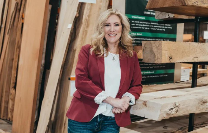 A woman in a red jacket is standing in front of a pile of wood.