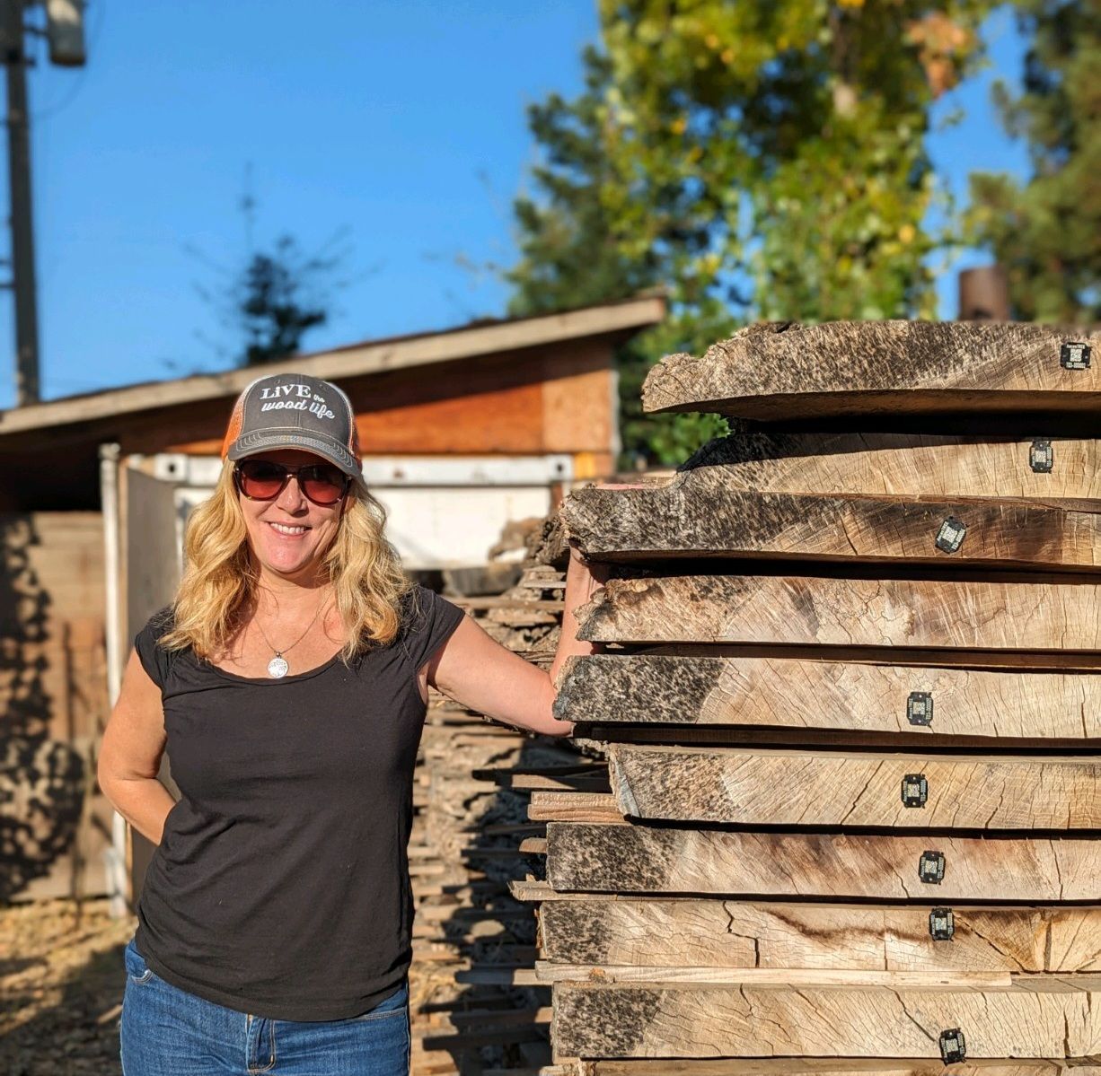 A woman wearing a hat and sunglasses is standing next to a pile of wood.