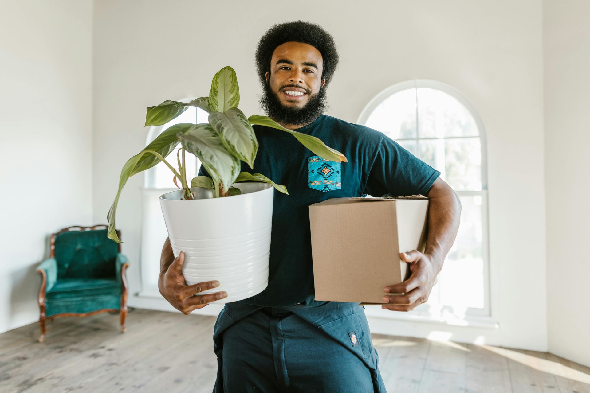 Man holding a potted plant and a box in a bright room. Smiling.