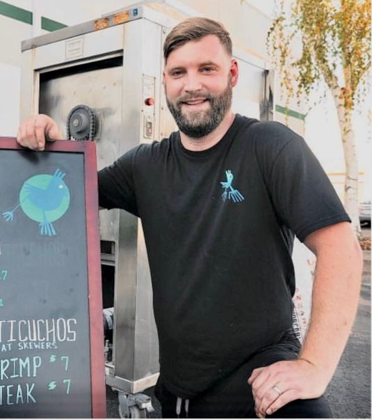 A man in a black shirt is standing next to a sign that says chichos