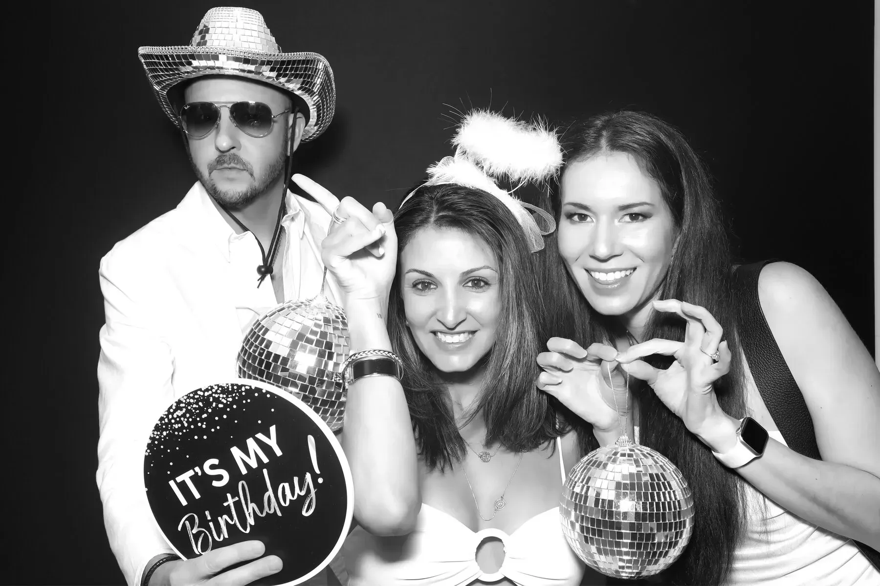 Three people at a birthday party, smiling and posing with props like disco balls and a 